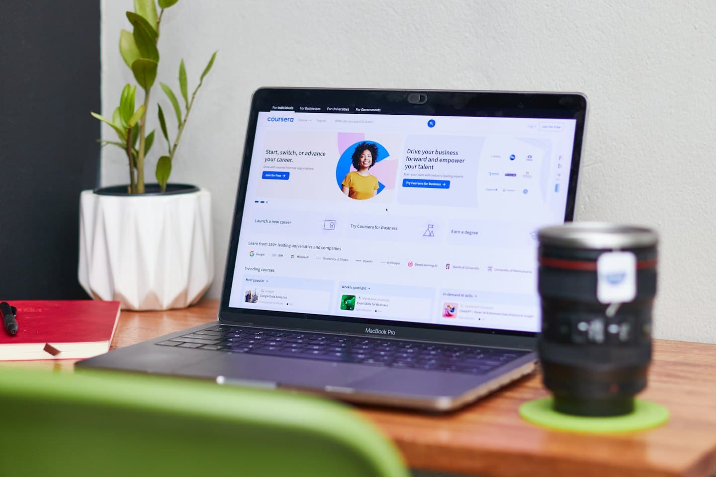 MacBook Pro zobrazujúci webstránku Coursera na drevenom stole s rastlinou.